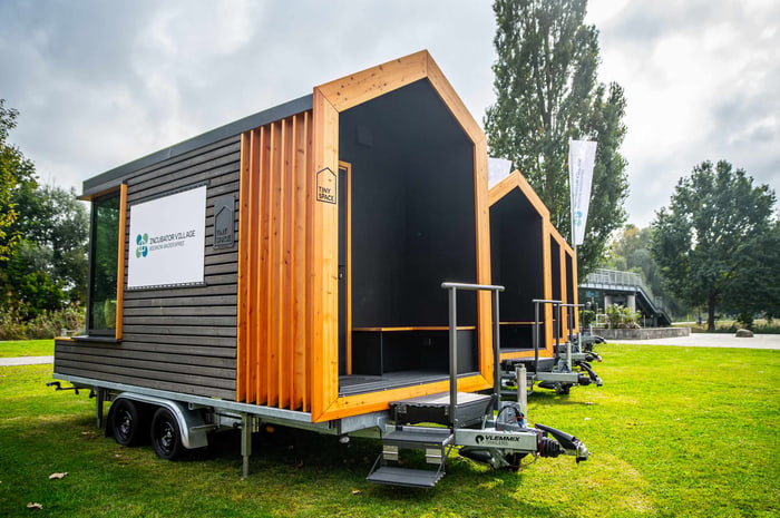Mehrere Tiny Houses auf Anhängern stehen auf einer grünen Wiese unter bewölktem Himmel.