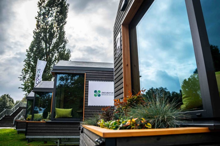 Mehrere Tiny Houses aus Holz mit großen Fenstern und Pflanzkästen unter einem bewölkten Himmel.
